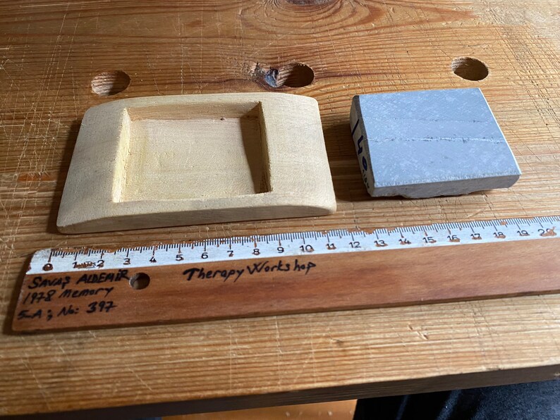 May include: A wooden tray with a rectangular cutout and a gray stone block. The tray is 10 inches long and the stone block is 3 inches wide. The ruler is labeled "Therapy Workshop" and "SAVAŞ ALDEMIR 1978 Memory 5A; No: 397".