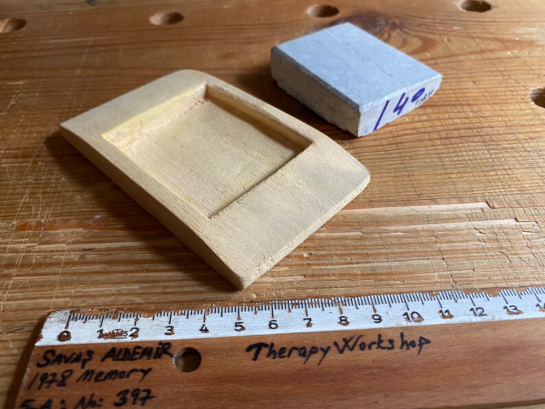May include: A light yellow wooden tray with a rectangular recess, a gray rectangular block, and a wooden ruler with the text "Therapy Works hop" and "SAVAŞ ALDEMİR 1978 Memory SA: No: 397".