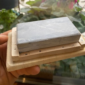 Peut inclure: Une pierre &agrave; aiguiser grise avec une base en bois. La base a une s&eacute;rie de petits trous autour du bord.