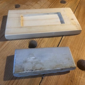 May include: Two rectangular ceramic tiles, one white with a recessed rectangular opening and the other a light grey with a rough texture.