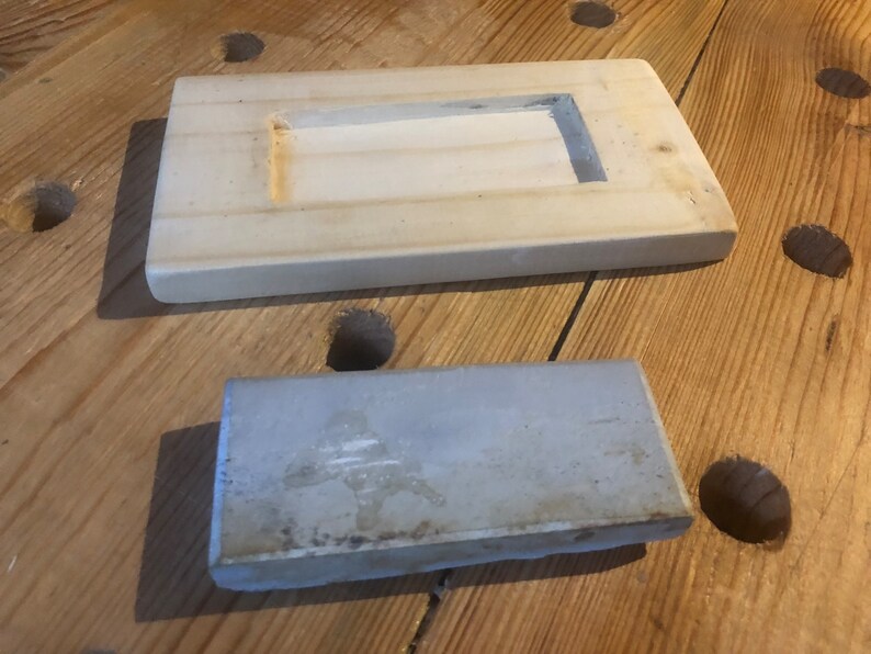 May include: Two rectangular ceramic tiles, one white with a recessed rectangular opening and the other a light grey with a rough texture.