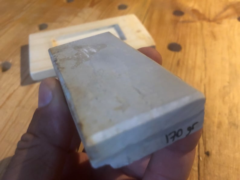 May include: A grey rectangular sharpening stone with a white edge and the number "170 gr" written on the side.