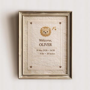 May include: Framed birth announcement featuring a beige background with a stitched border. The text reads "Welcome, OLIVER" above the date, time, weight (8 lbs), and height (20 inches). A lion face is embroidered at the top.