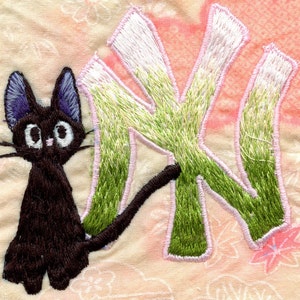 May include: Embroidered black cat with a long tail, sitting next to a green and white embroidered letter "N".