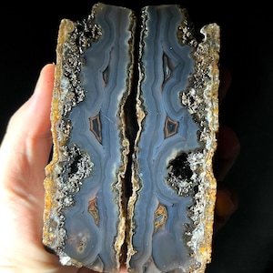 Puede incluir: Dos mitades de una geoda con un patrón de ágata azul y marrón. La geoda está cortada por la mitad y muestra los intrincados patrones de la ágata.