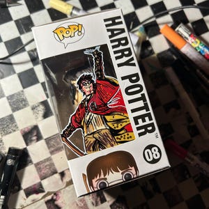 May include: A white Funko Pop box featuring Harry Potter number 08. The box displays a stylized illustration of Harry Potter in a red robe with a wand raised, along with the text Harry Potter and the number 08. A small character face is visible.