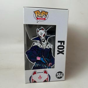 以下が含まれることがあります： ビデオゲーム「ペルソナ5」のキャラクター、フォックスをフィーチャーしたFunko Pop! Gamesの箱。白い箱にはPop! Gamesのロゴと、ダークブルーと白の衣装を着たフィギュアが見える窓があります。番号584が箱に印刷されています。