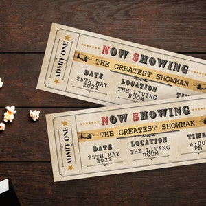 Peut inclure: Deux billets de cin&eacute;ma de style vintage avec le texte "Now Showing The Greatest Showman" sur une surface en bois brun. Les billets ont une date du 25 mai 2022, un lieu "The Living Room" et une heure de 16h00.