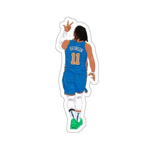 May include: A basketball player wearing a blue jersey with the name "Brunson" and the number "11" on the back. The player is wearing green and white trainers and has their hand raised in the air.