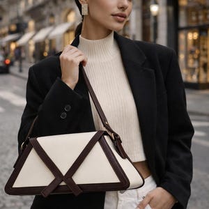 Peut inclure: Sac &agrave; main g&eacute;om&eacute;trique cr&egrave;me et marron fonc&eacute;. La personne porte un blazer noir, un col roul&eacute; cr&egrave;me et un jean blanc. En arri&egrave;re-plan, une rue de la ville avec des b&acirc;timents.