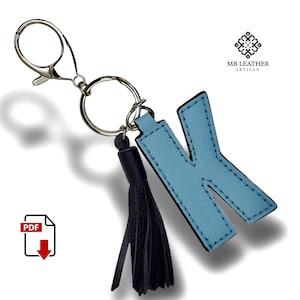 May include: A light blue leather keychain with the letter K and a black tassel. The keychain is attached to a silver key ring. The text "MB LEATHER ARTISAN" is visible in the top right corner of the image. The image also includes a PDF download icon.