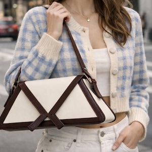 Peut inclure: Un sac &agrave; main cr&egrave;me avec des accents en cuir marron fonc&eacute; et un design g&eacute;om&eacute;trique. Le sac est port&eacute; par une personne portant un cardigan &agrave; carreaux bleu et blanc et un jean blanc.