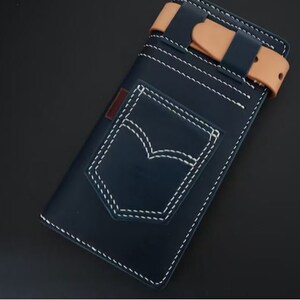 May include: A navy blue leather wallet with a white stitched pocket detail, resembling a classic jean pocket. The wallet has a tan leather strap with a buckle closure.