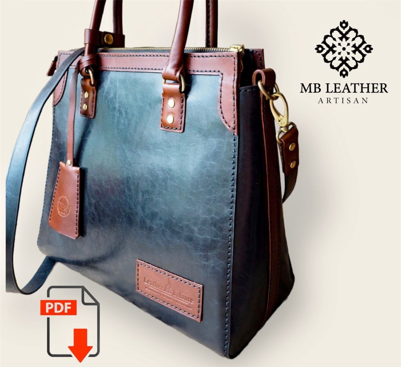 Pode incluir: Bolsa de couro artesanal com corpo azul-esverdeado escuro e detalhes marrons. A bolsa possui uma al&ccedil;a superior, uma al&ccedil;a de ombro remov&iacute;vel e uma etiqueta de couro. A marca "MB LEATHER ARTISAN" &eacute; vis&iacute;vel.