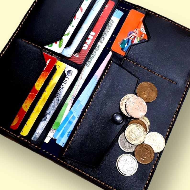 May include: Black leather wallet with multiple card slots and a zippered pocket. The wallet is open and filled with credit cards and coins.
