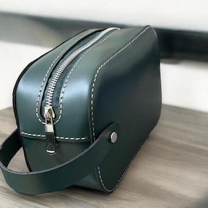 May include: A dark green leather travel bag with a zip closure and a top handle. The bag has white stitching around the edges.