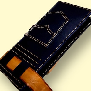 May include: A black leather wallet with a brown leather strap. The wallet has a pocket on the front with a stitched design that resembles a jean pocket.