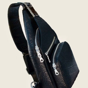 Peut inclure: Sac &agrave; bandouli&egrave;re en cuir noir avec plusieurs compartiments &agrave; fermeture &eacute;clair et une boucle argent&eacute;e.