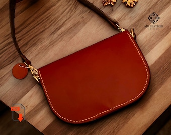 May include: A brown leather handbag with a curved shape and a gold clasp. The bag has a long strap and a white stitch detail around the edges. The bag is on a wooden surface.