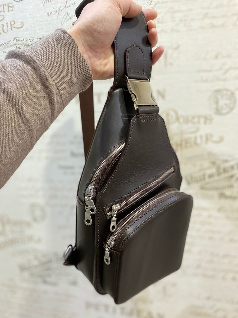 Peut inclure: Un sac &agrave; bandouli&egrave;re en cuir marron avec plusieurs compartiments &agrave; fermeture &eacute;clair et une boucle argent&eacute;e.