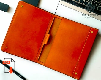 May include: Orange leather notebook cover with a flap and a pocket for a pen. The cover has stitching around the edges and brass rivets. The text "MB LEATHER ARTISAN" is printed on the cover.