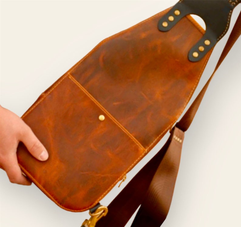 May include: A brown leather crossbody bag with a flap closure and a long adjustable strap. The bag has a small pocket on the front and a brass button.