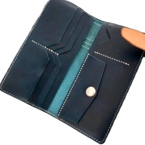 May include: A dark blue leather wallet with a light brown leather strap and a silver button. The wallet has multiple compartments and pockets.