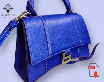 May include: A small, bright blue leather handbag with a gold clasp and a top handle. The bag has a  stitched design and a  'B' logo on the front.  The bag is  made by MB Leather Artisan.