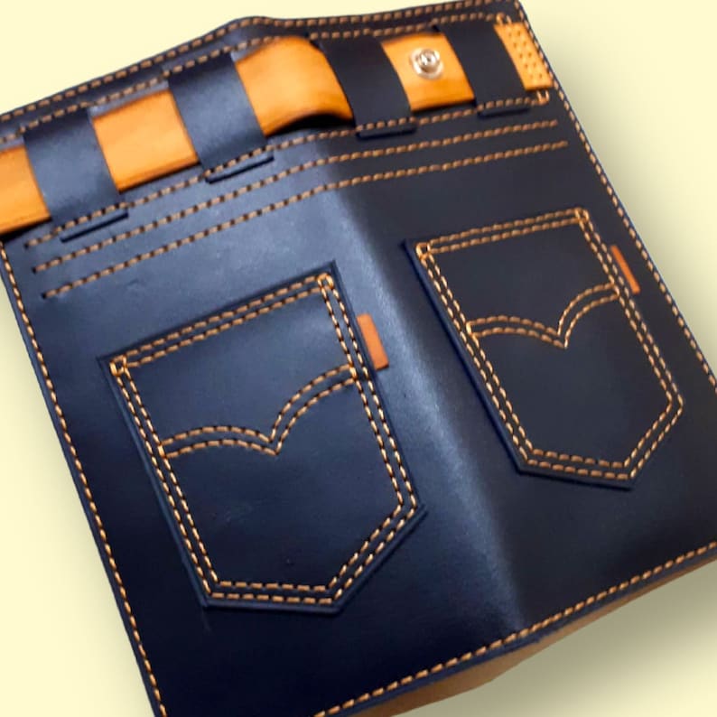 May include: A blue leather wallet with a denim design. The wallet has two pockets with orange stitching and a brown leather strap with a button closure.