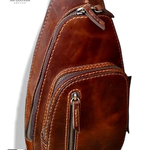 Könnte beinhalten: Eine braune Leder-Umhängetasche mit mehreren Reißverschlussfächern und einem Klappverschluss. Die Tasche hat ein genähtes Design und einen braunen Lederriemen.