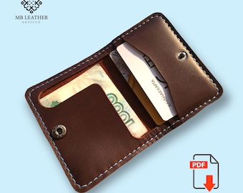 May include: A brown leather wallet with a blue stitch detail. The wallet is open and has a card and cash inside. The wallet has a snap closure and the text "MB LEATHER ARTISAN" is visible.