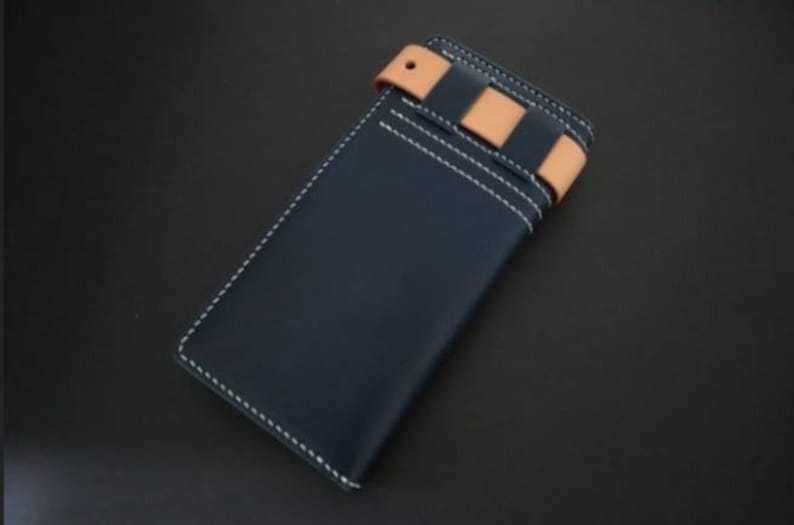 May include: A dark blue leather wallet with a tan leather strap and white stitching. The strap has a decorative pattern of tan leather strips.