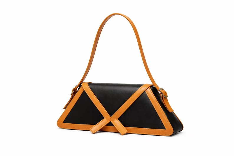 Peut inclure: Un sac &agrave; main noir et beige de forme triangulaire. Le sac est orn&eacute; de bordures et de lani&egrave;res en cuir beige, contrastant avec le corps noir. La bandouli&egrave;re est longue et fine, et le sac se ferme par une boucle.
