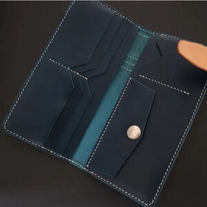 May include: A dark blue leather wallet with multiple card slots and a large bill compartment. The wallet has a light brown leather strap and a silver button closure.
