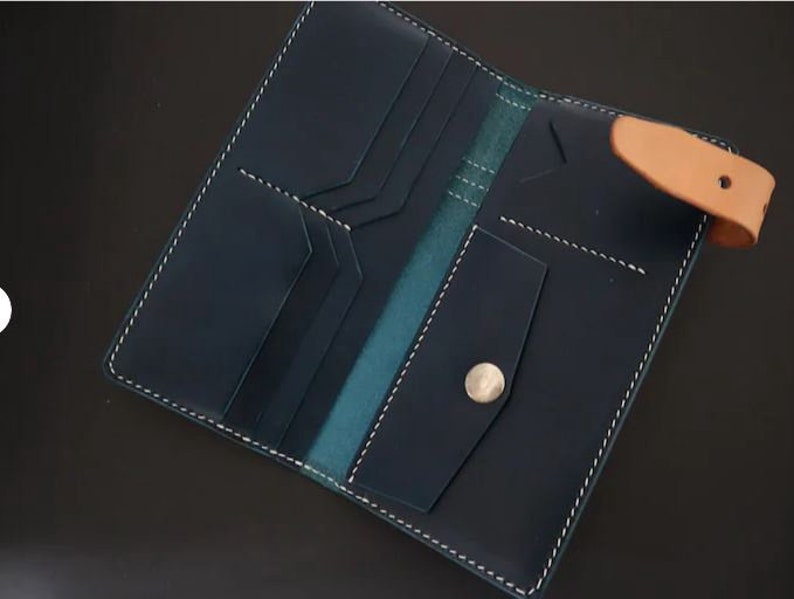 May include: A dark blue leather wallet with multiple card slots and a large bill compartment. The wallet has a light brown leather strap and a silver button closure.