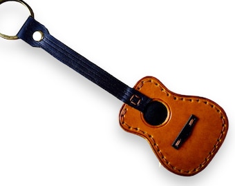 May include: A brown leather guitar keyring with a black leather strap and a gold key ring.