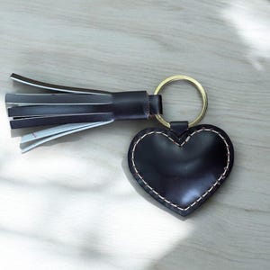 May include: A black leather heart-shaped keyring with a gold ring and a black and white tassel.