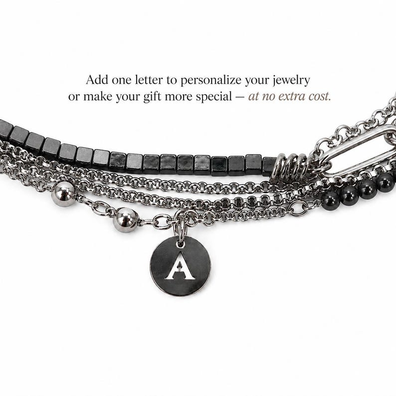 Puede incluir: Una pulsera de cadenas m&uacute;ltiples en color gris plomo con una fila de cuentas cuadradas, esferas met&aacute;licas redondas y un dije circular grabado con la letra A. El texto superior dice: Add one letter to personalize your jewelry or make your gift more special &mdash; at no extra cost.