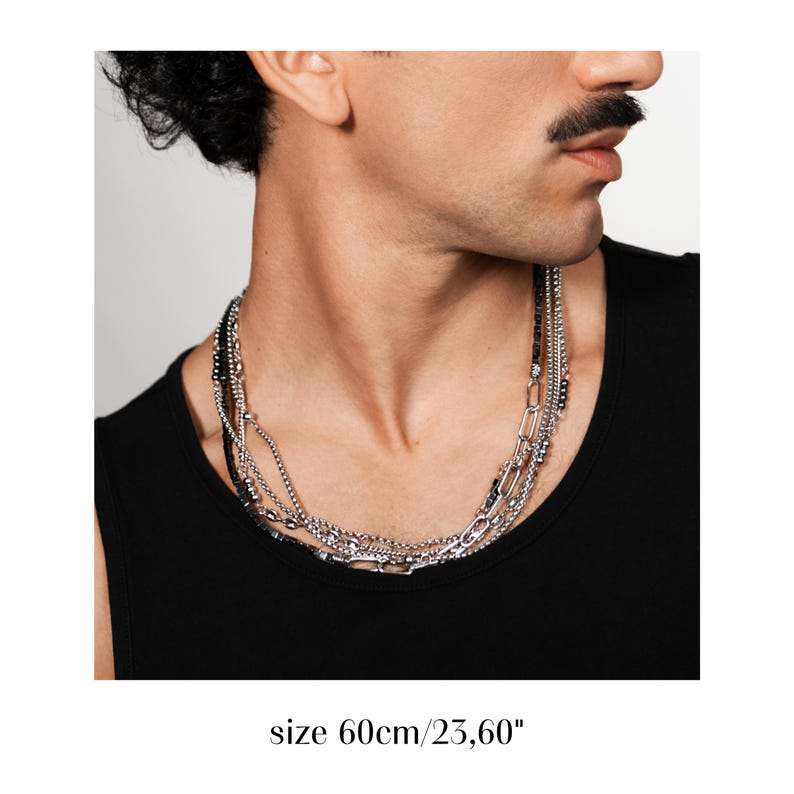 Puede incluir: Un collar de capas en tono plateado que presenta m&uacute;ltiples estilos de cadena, incluyendo una cadena de eslabones gruesos y hebras de cuentas m&aacute;s finas, con una longitud de 60 cm. El collar se lleva al cuello y tiene un acabado met&aacute;lico.