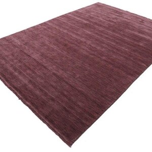 May include: A rectangular, plum-colored rug with a textured surface. The rug has a simple design with a solid color and a soft, inviting appearance. The rug is suitable for a living room or bedroom.