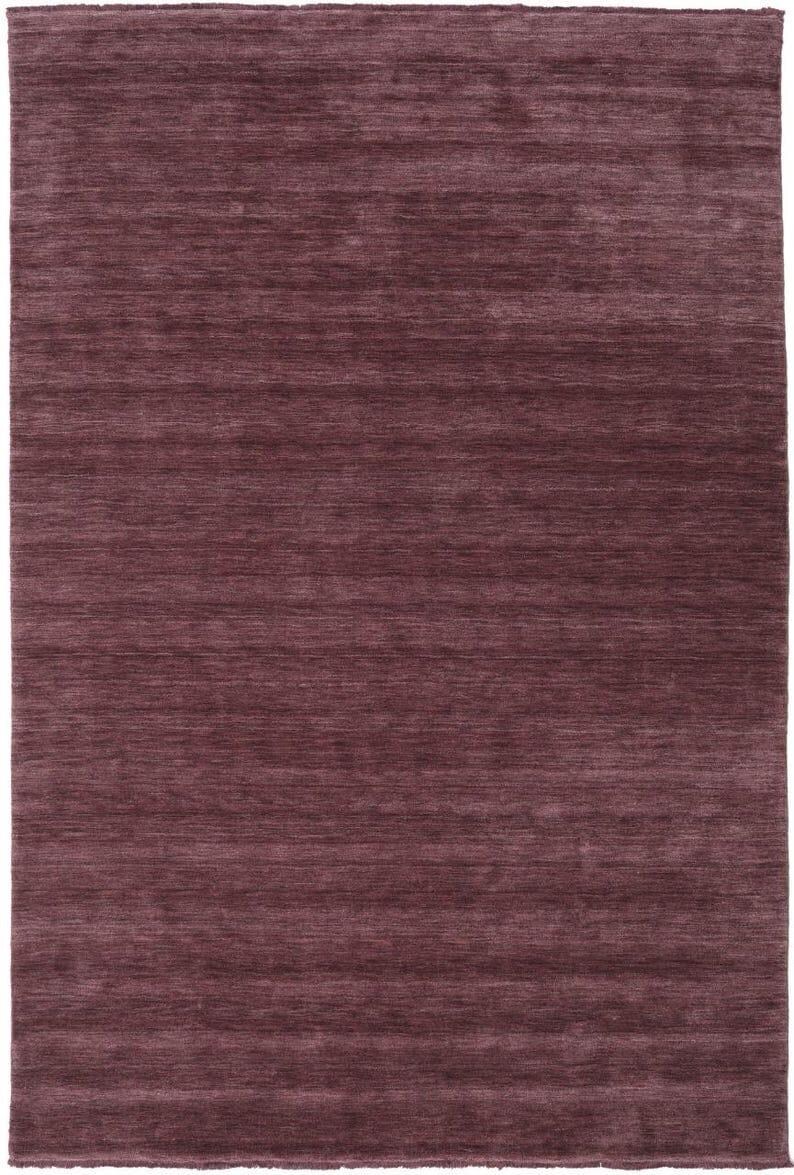May include: A rectangular rug in a deep burgundy color. The rug has a textured appearance with horizontal lines running across its surface. The overall design is simple and modern, suitable for various interior styles.