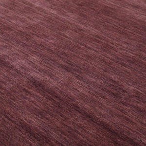 May include: Close-up of a burgundy-colored rug with a textured surface. The rug's fibers are arranged in a diagonal pattern, creating a sense of depth and movement. The color is a deep, rich shade of red-purple.