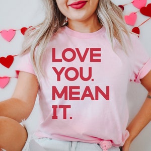 May include: Pink t-shirt with the text "LOVE YOU. MEAN IT." in red.