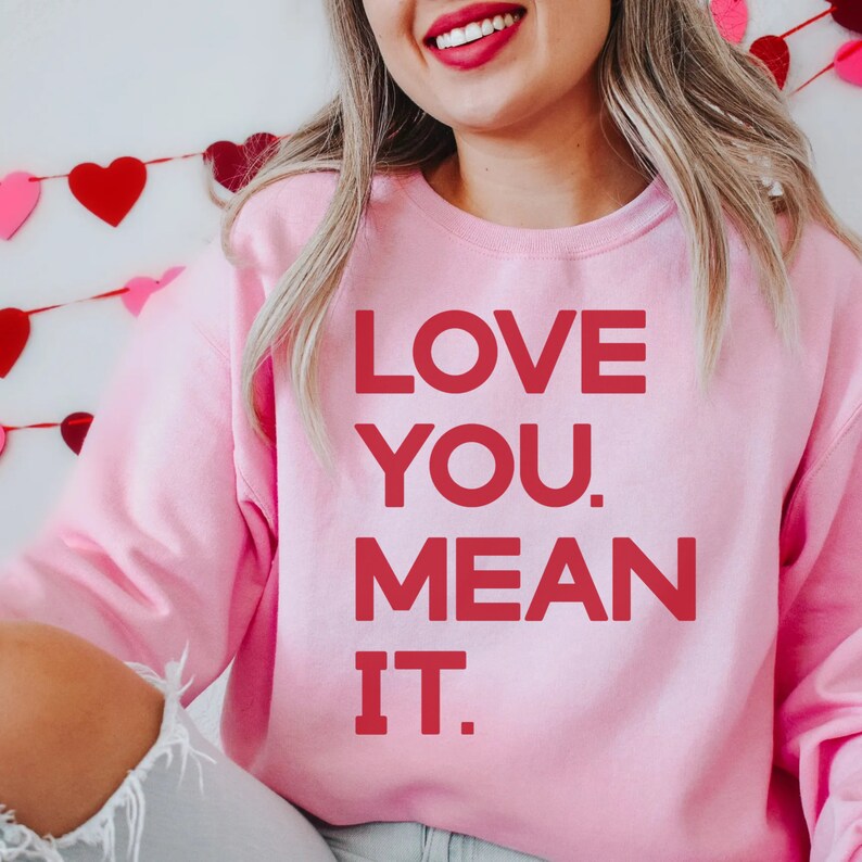 May include: Pink sweatshirt with the text "LOVE YOU. MEAN IT." in red letters.