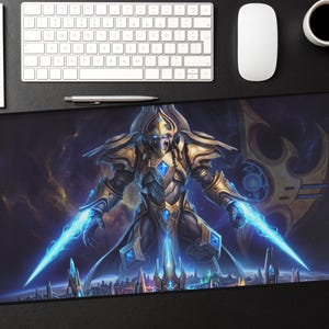 Pode incluir: Um grande tapete de rato retangular com uma ilustração detalhada de um guerreiro futurista com lâminas de energia azul brilhante. O guerreiro está vestido com uma armadura dourada e azul, contra um fundo cósmico. Um teclado, rato, caneta, bloco de notas e chávena de café também são visíveis.