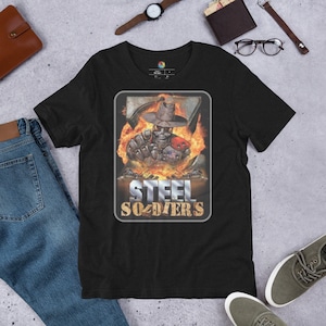 Peut inclure: T-shirt noir avec un graphique d'un robot portant un chapeau et tenant un fusil. Le robot est entouré de flammes. Le texte "STEEL SOLDIERS" est imprimé sous le robot.