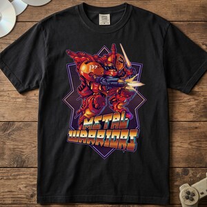 Puede incluir: Una camiseta negra de manga corta con un gráfico de una figura robótica roja que sostiene un arma y una hoja brillante. Debajo de la figura, el texto METAL WARRIORS está impreso en una fuente estilizada y multicolor sobre una forma geométrica morada.