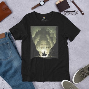Może przedstawiać: Czarny T-shirt z grafiką przedstawiającą sylwetkę osoby jadącej konno w kierunku gigantycznej, cienistej postaci. Tekst "Shadow of the Colossus" jest nadrukowany pod obrazkiem.