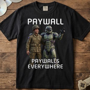 May include: A black short-sleeve t-shirt featuring a graphic of a soldier in a tan uniform standing next to a green armored futuristic character. The text PAYWALL is printed above the figures, and PAYWALLS EVERYWHERE is printed below them.