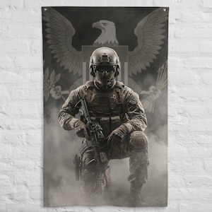 Pode incluir: Uma bandeira com um soldado ajoelhado, segurando um rifle, com uniforme e capacete de camuflagem. O fundo inclui um emblema de águia cinza e um escudo. A bandeira tem um acabamento fosco.